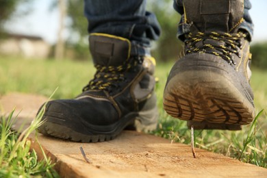 Careless worker stepping on nail in wooden plank outdoors, closeup