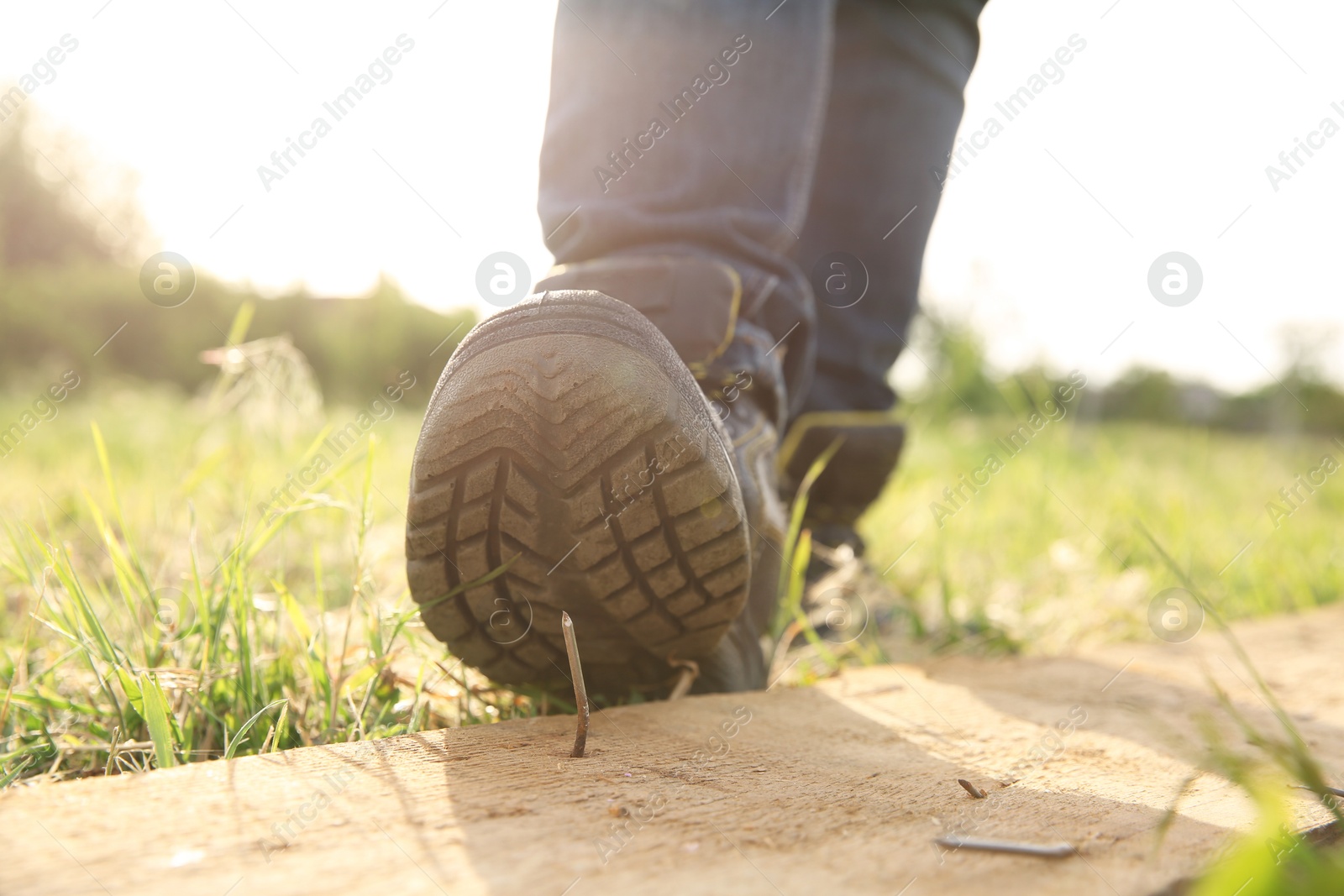 Photo of Careless worker stepping on nail in wooden plank outdoors, closeup