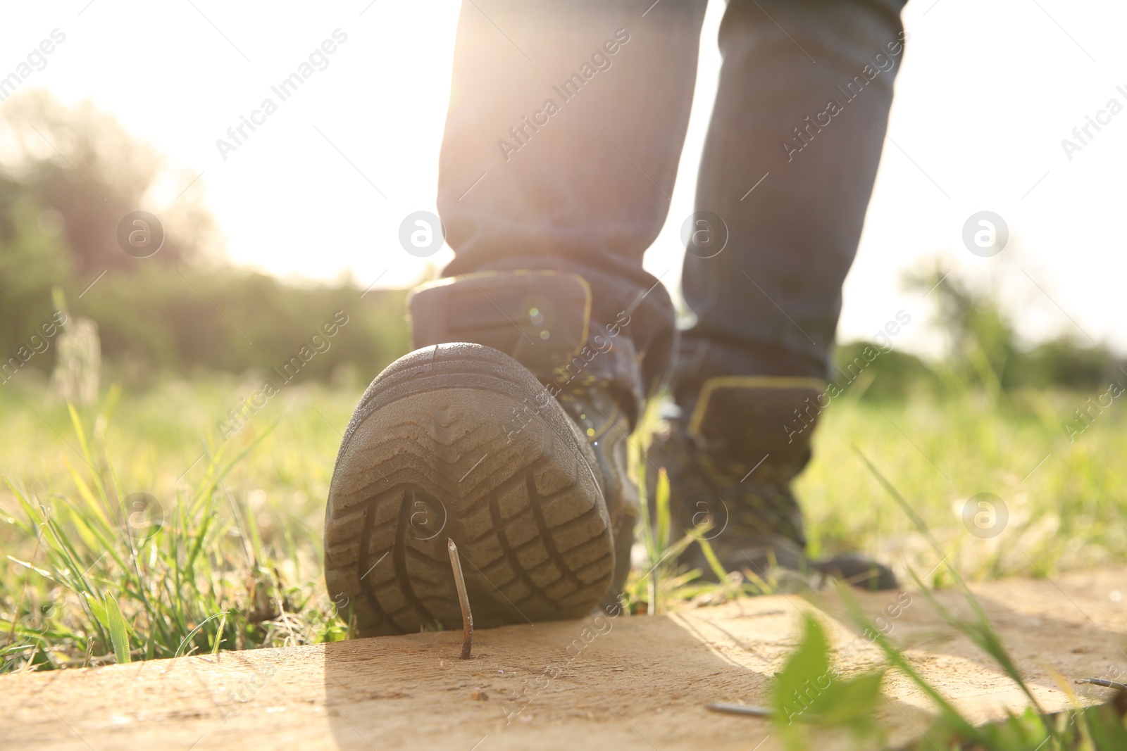 Photo of Careless worker stepping on nail in wooden plank outdoors, closeup