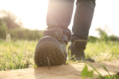 Careless worker stepping on nail in wooden plank outdoors, closeup