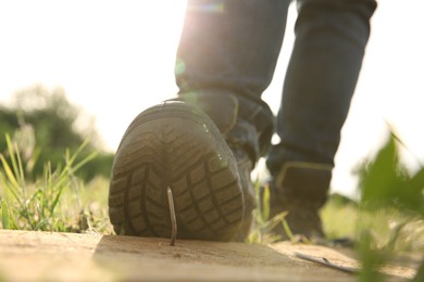 Careless worker stepping on nail in wooden plank outdoors, closeup