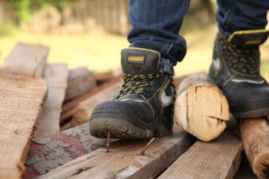 Photo of Careless worker stepping on nail in wooden plank outdoors, closeup