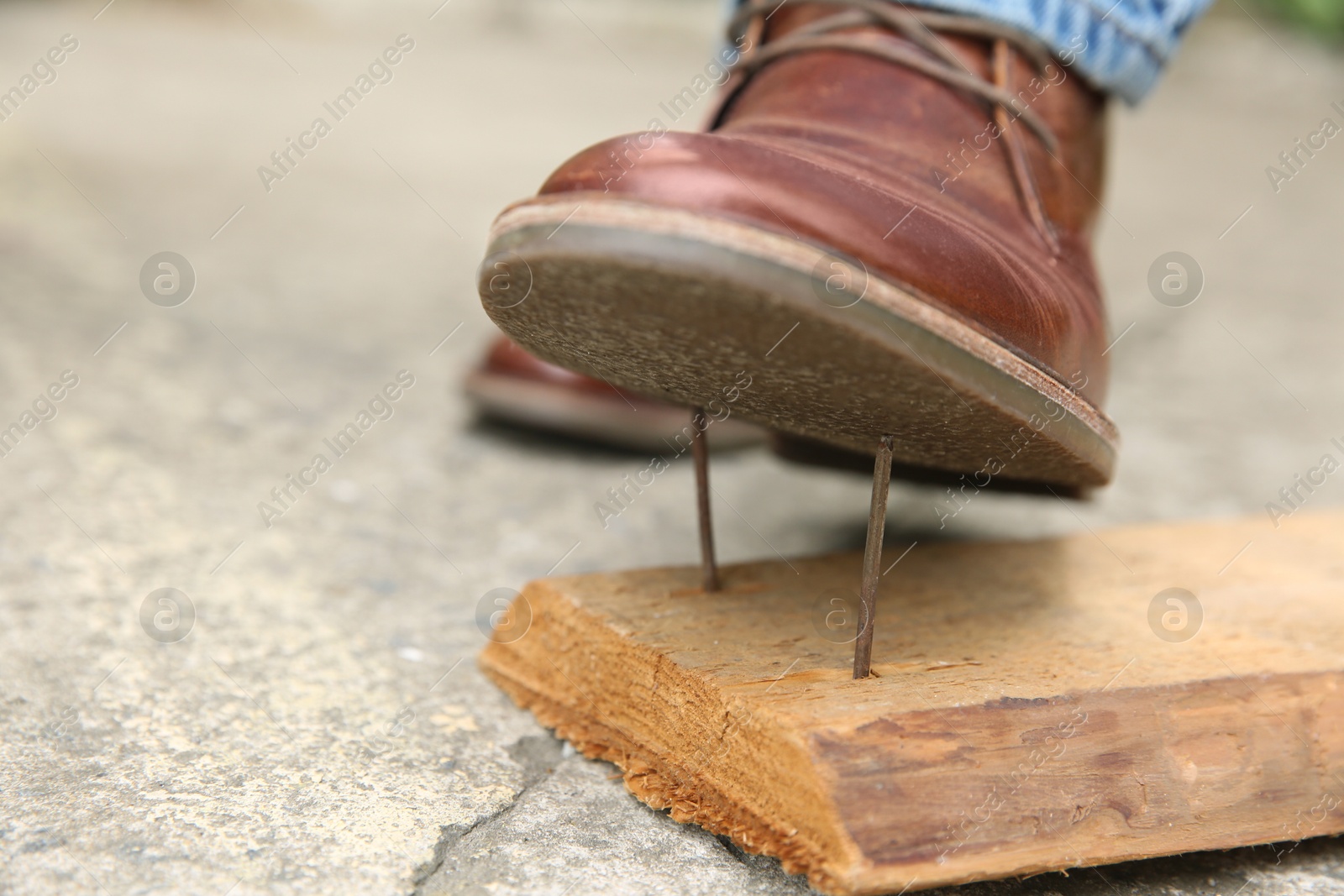 Photo of Careless man stepping on nails in wooden plank outdoors, closeup. Space for text