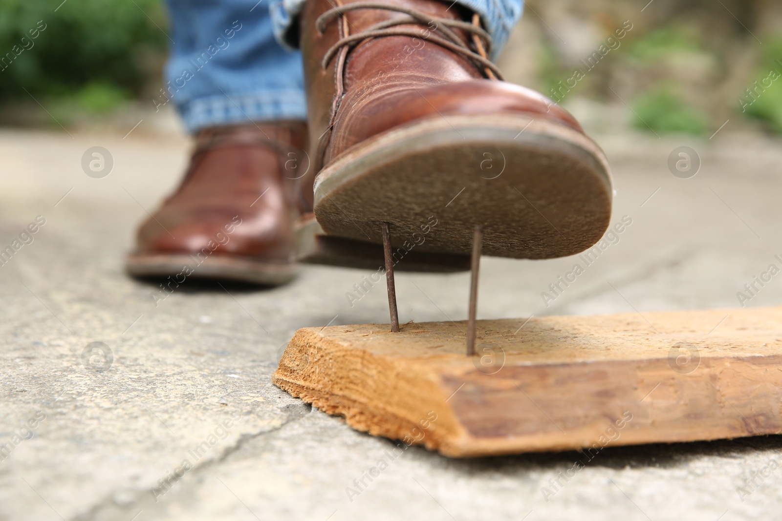 Photo of Careless man stepping on nails in wooden plank outdoors, closeup