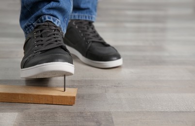 Photo of Careless man stepping on nail in wooden plank, closeup. Space for text
