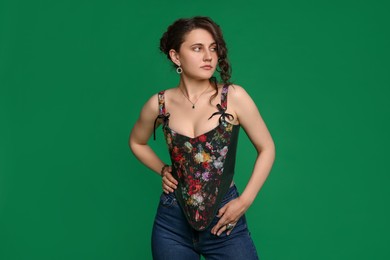 Beautiful woman in stylish corset posing on green background