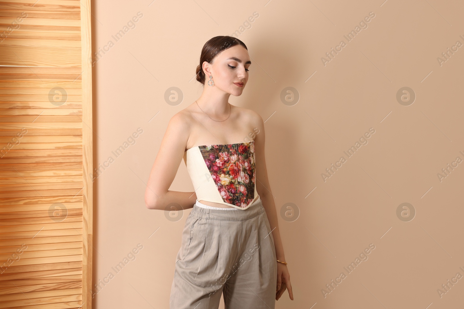 Photo of Beautiful young woman in stylish corset near beige wall