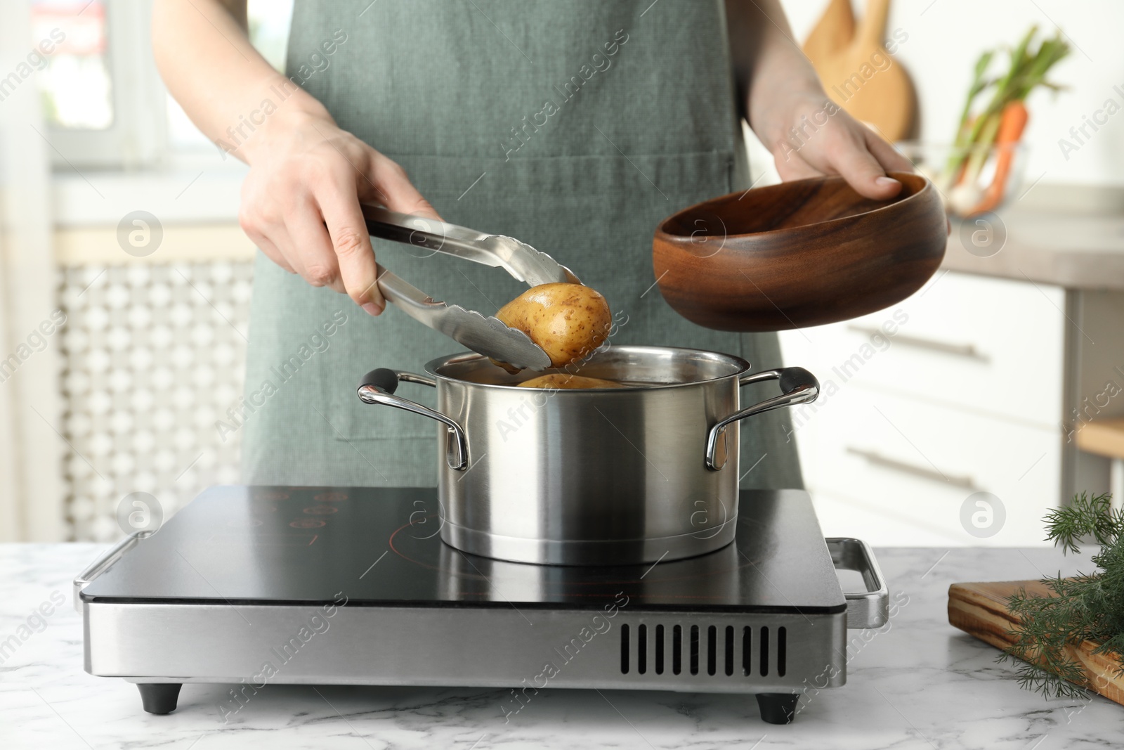 Photo of Woman putting potato into metal pot on stove, closeup