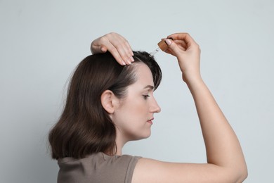 Photo of Hair loss problem. Woman applying serum onto hairline on light background