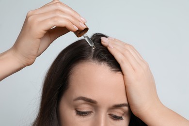 Photo of Hair loss problem. Woman applying serum onto hairline on light background