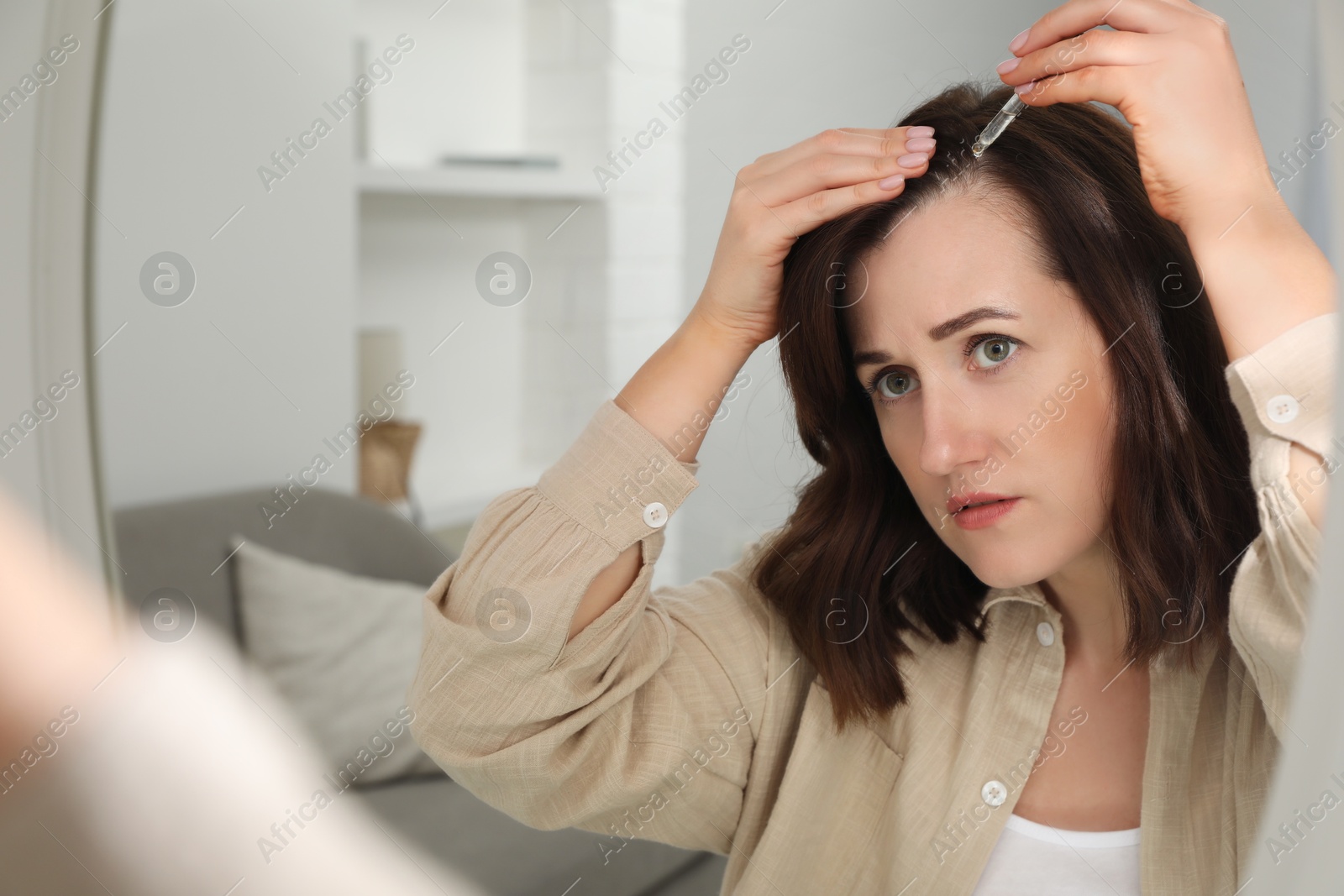 Photo of Hair loss problem. Woman applying serum onto hairline near mirror at home