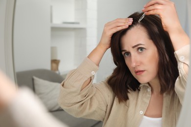 Hair loss problem. Woman applying serum onto hairline near mirror at home