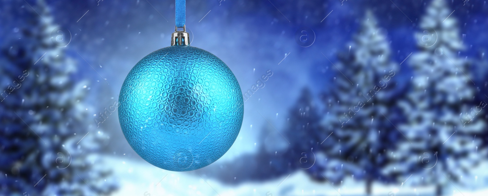 Image of Light blue Christmas ball against snowy forest, banner design. Space for text