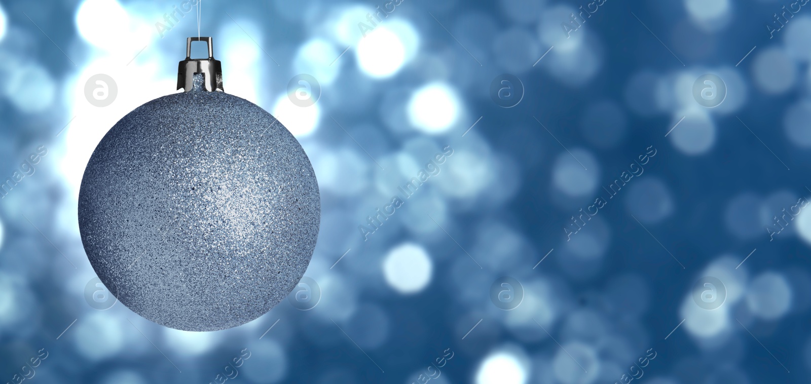 Image of Shiny Christmas ball against blurred blue background with bokeh effect. Banner design with space for text