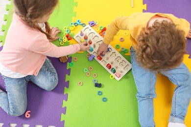 Photo of Cute little children playing with game Fishing for Numbers on puzzle mat, above view. Kindergarten activities for learning mathematics