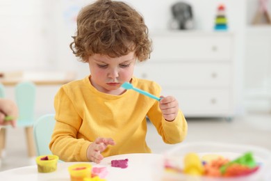 Cute little boy modeling from plasticine at white table in kindergarten