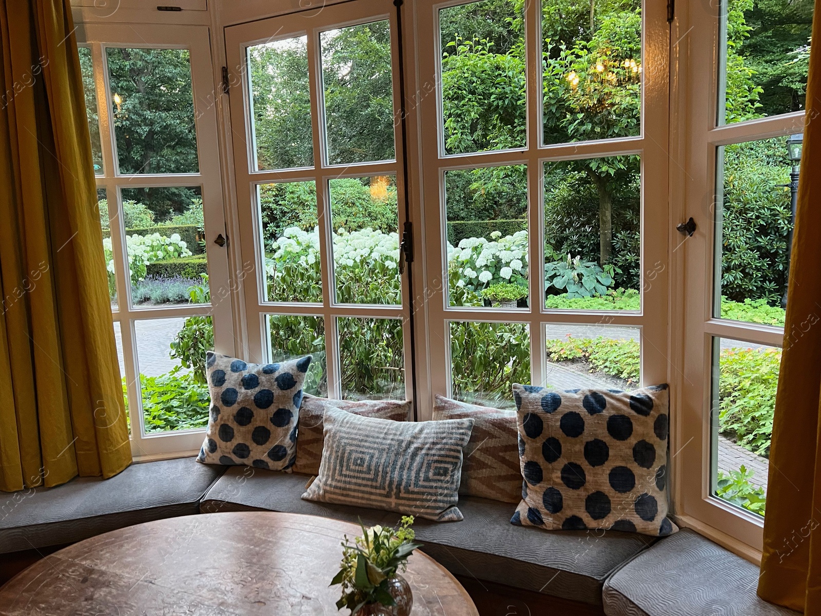 Photo of Wooden table near bay window seat with cushions in cozy room. Interior design