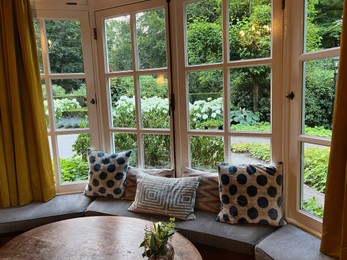 Photo of Wooden table near bay window seat with cushions in cozy room. Interior design