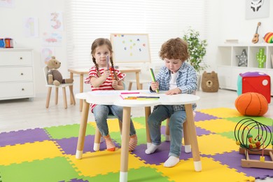 Photo of Cute little children drawing with colorful pencils at white table in kindergarten