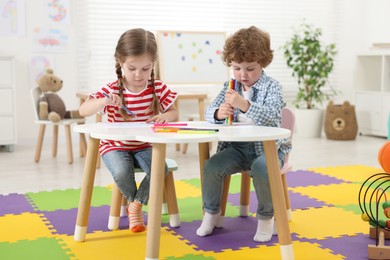 Cute little children drawing with colorful pencils at white table in kindergarten