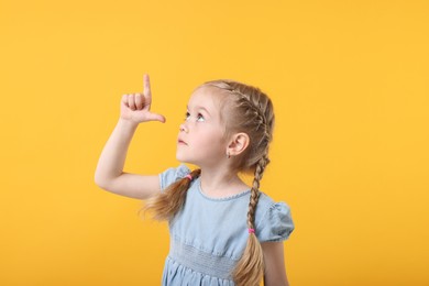 Photo of Cute little girl pointing at something on orange background