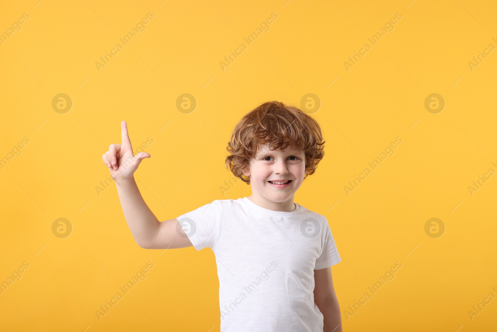 Photo of Cute little boy pointing at something on orange background