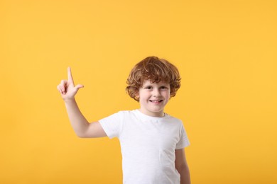 Cute little boy pointing at something on orange background