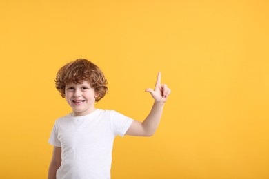 Cute little boy pointing at something on orange background, space for text