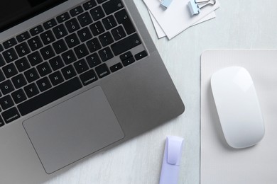 Photo of Wireless mouse with mousepad, stationery and laptop on light wooden table, flat lay