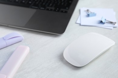 Photo of Wireless mouse, stationery and laptop on light wooden table, closeup