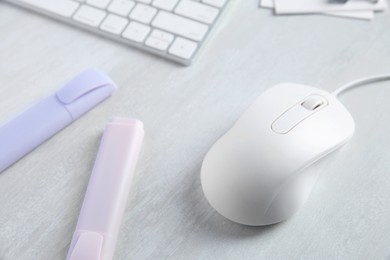 Photo of Wired mouse, stationery and computer keyboard on light wooden table, closeup