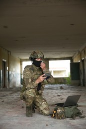 Military mission. Soldier in uniform with drone controller and laptop inside abandoned building