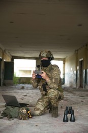 Photo of Military mission. Soldier in uniform with drone controller, laptop and binoculars inside abandoned building