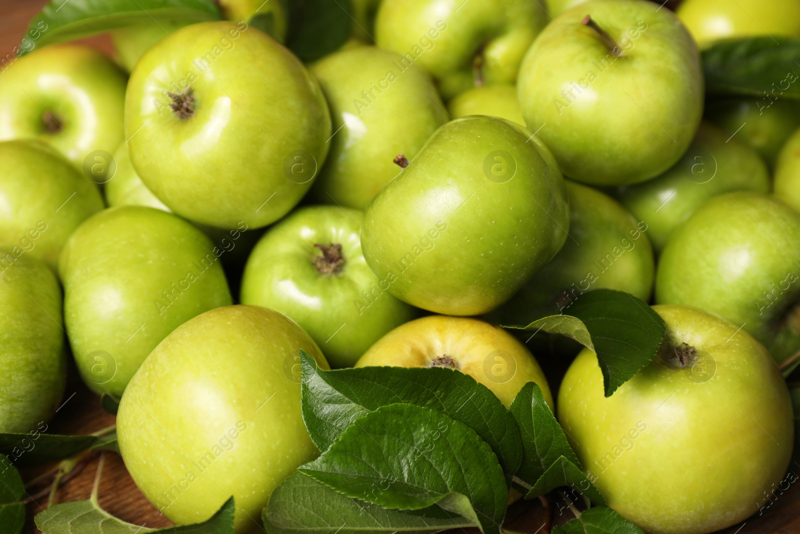 Photo of Fresh ripe green apples with leaves on wooden table, closeup