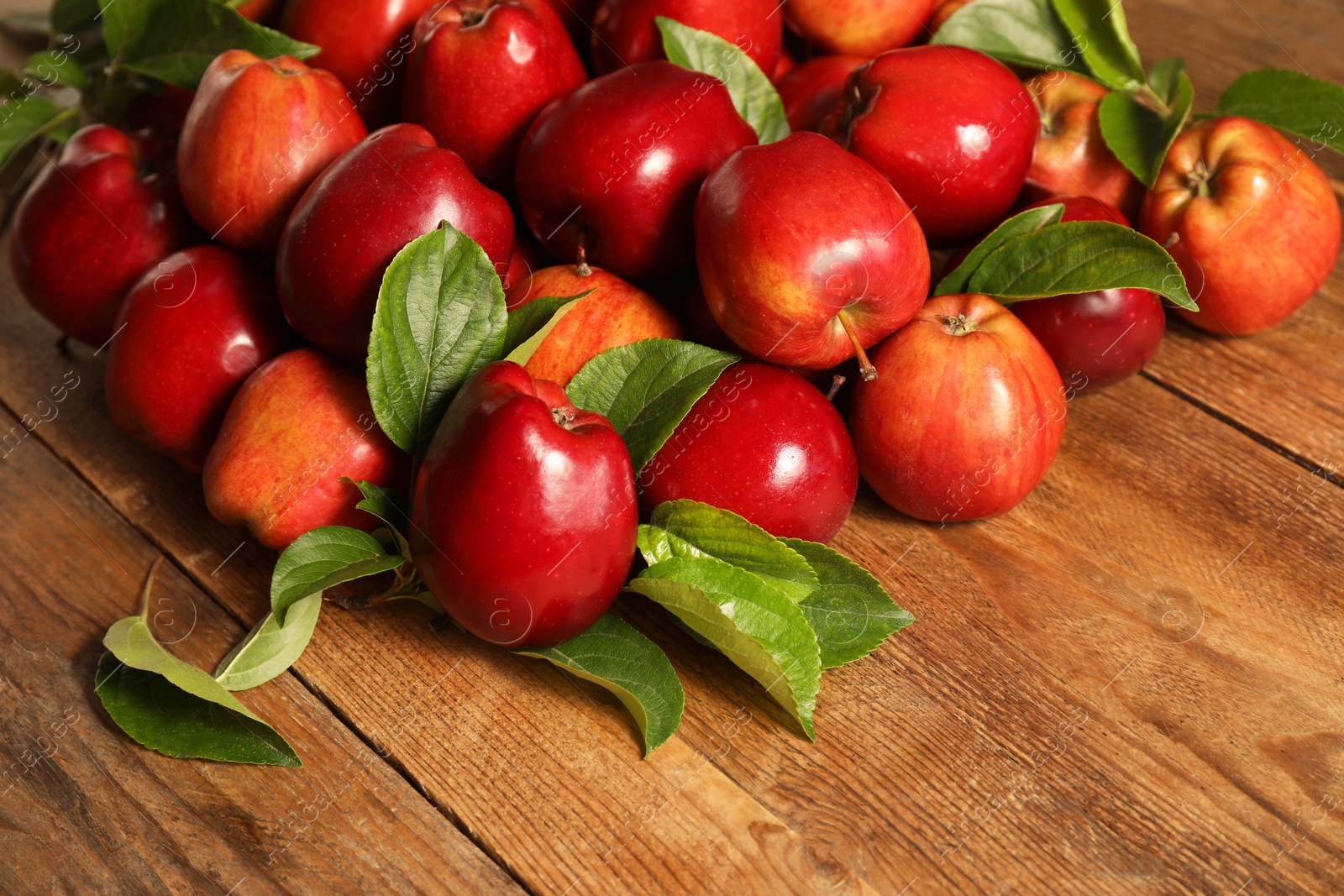 Photo of Fresh ripe red apples with leaves on wooden table. Space for text