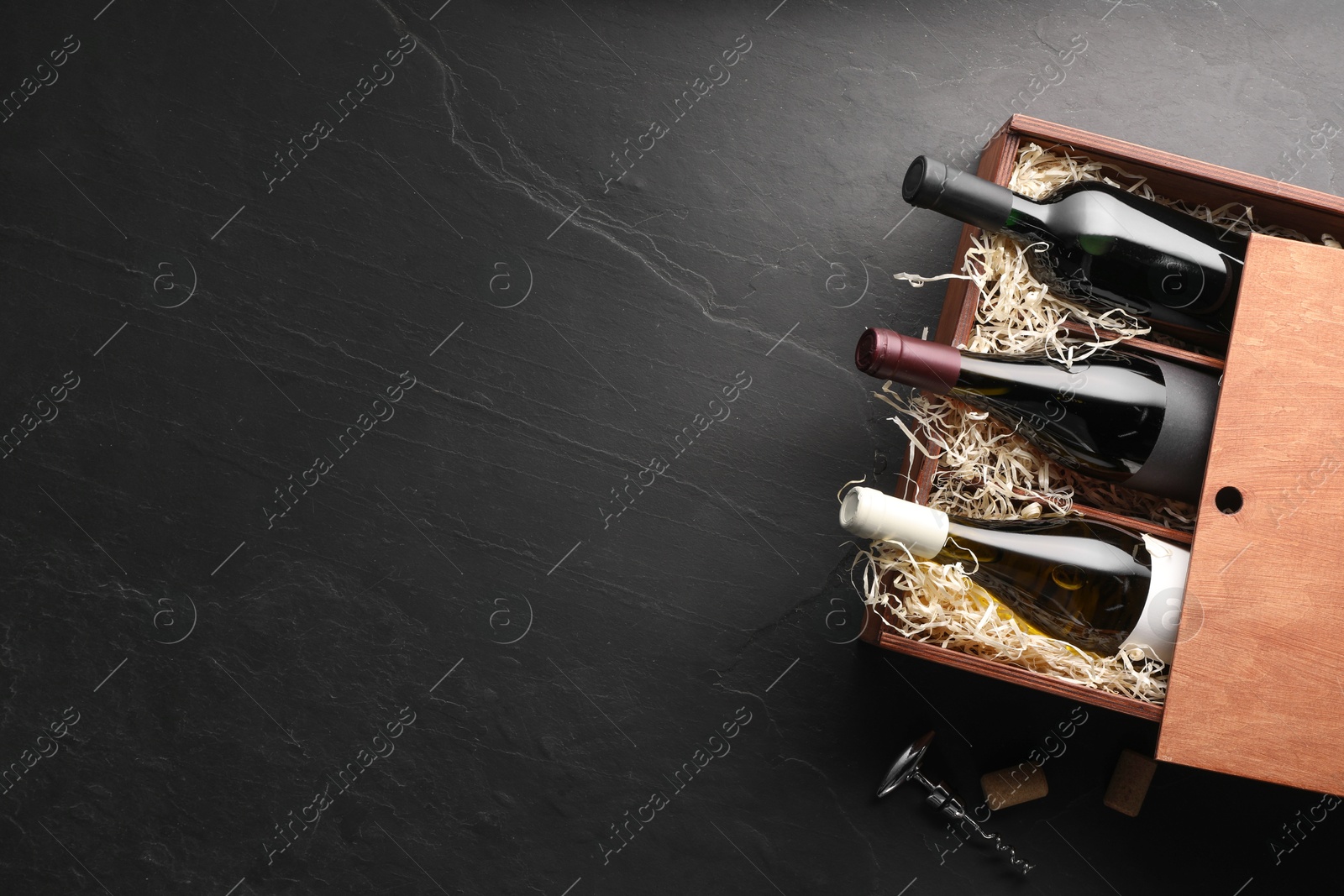 Photo of Box with wine bottles and corkscrew on dark textured table, top view. Space for text