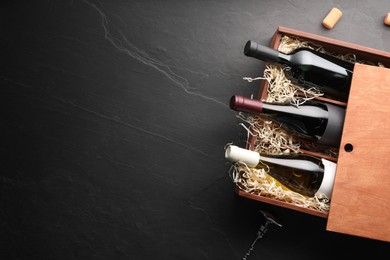 Photo of Box with wine bottles, corkscrew and corks on dark textured table, flat lay. Space for text