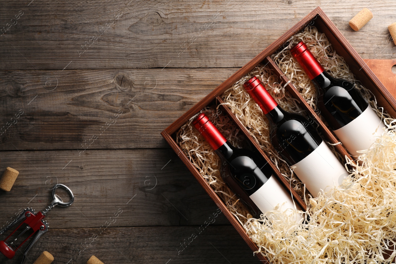 Photo of Box with wine bottles, corkscrew and corks on wooden table, flat lay. Space for text