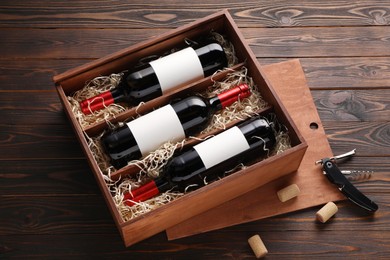 Photo of Box with wine bottles, corkscrew and corks on wooden table, above view