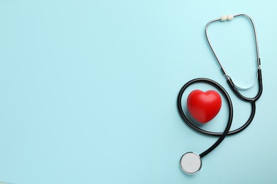 Photo of Stethoscope and red heart on light blue background, top view. Space for text