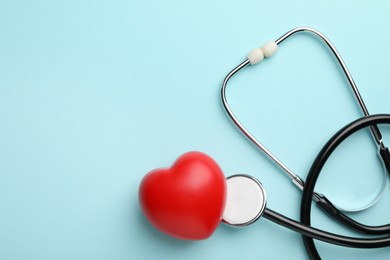 Photo of Stethoscope and red heart on light blue background, top view. Space for text