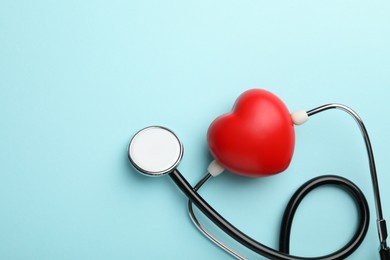 Photo of Stethoscope and red heart on light blue background, top view. Space for text