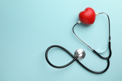 Stethoscope and red heart on light blue background, top view. Space for text