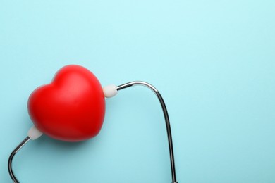 Photo of Stethoscope and red heart on light blue background, top view. Space for text