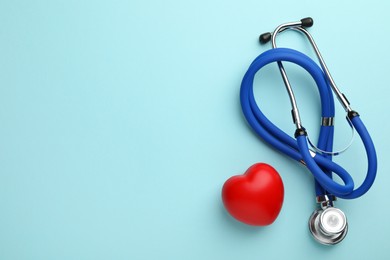 Photo of Stethoscope and red heart on light blue background, top view. Space for text