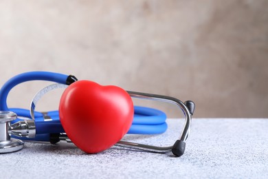 Photo of Stethoscope and red heart on grey stone table, closeup. Space for text