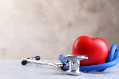 Photo of Stethoscope and red heart on grey stone table, closeup. Space for text