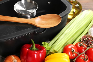 Photo of Black pot with glass lid, different products and wooden spoon on table