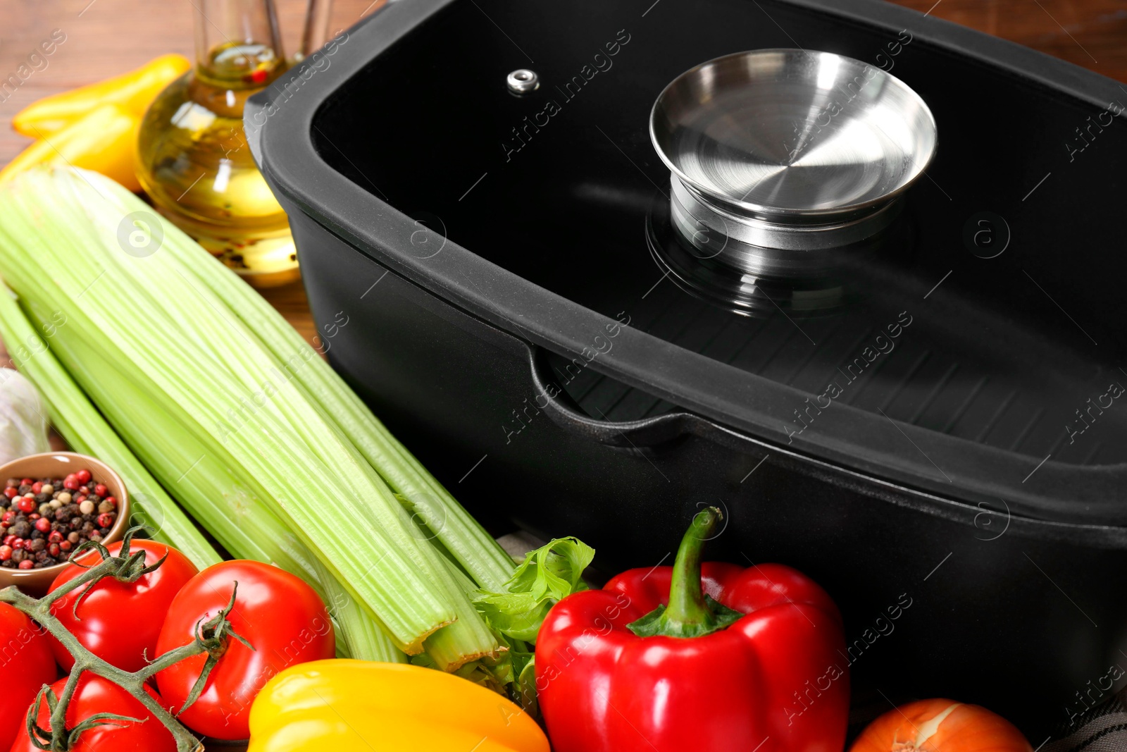 Photo of Black pot with glass lid, spices and vegetables on table