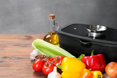 Photo of Black pot with glass lid, spices and vegetables on wooden table